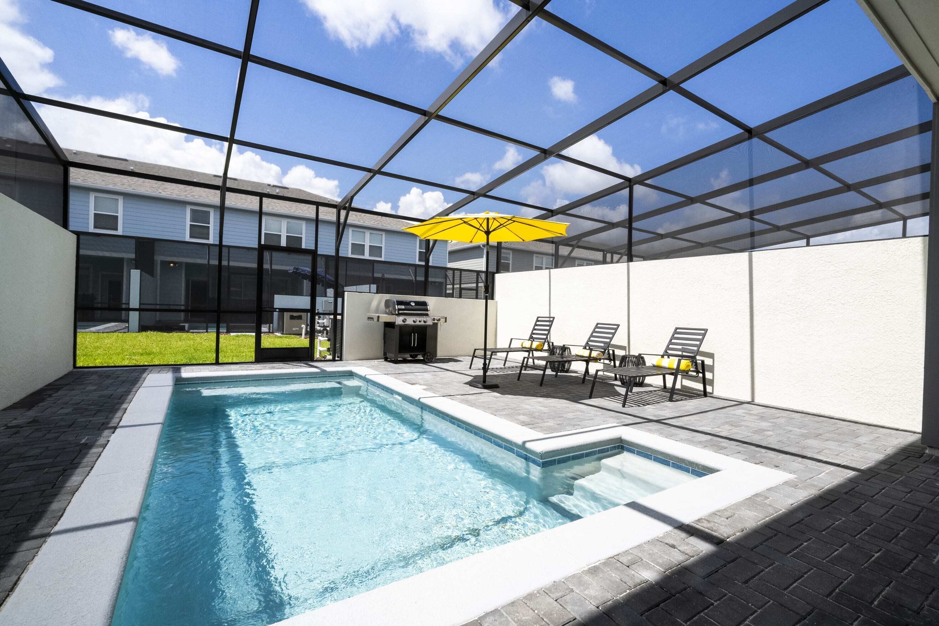 A modern indoor swimming pool with a glass ceiling, a barbecue area, and outdoor seating.