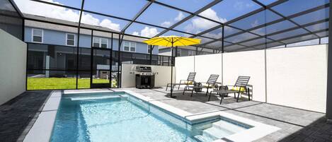 A modern indoor swimming pool with a glass ceiling, a barbecue area, and outdoor seating.