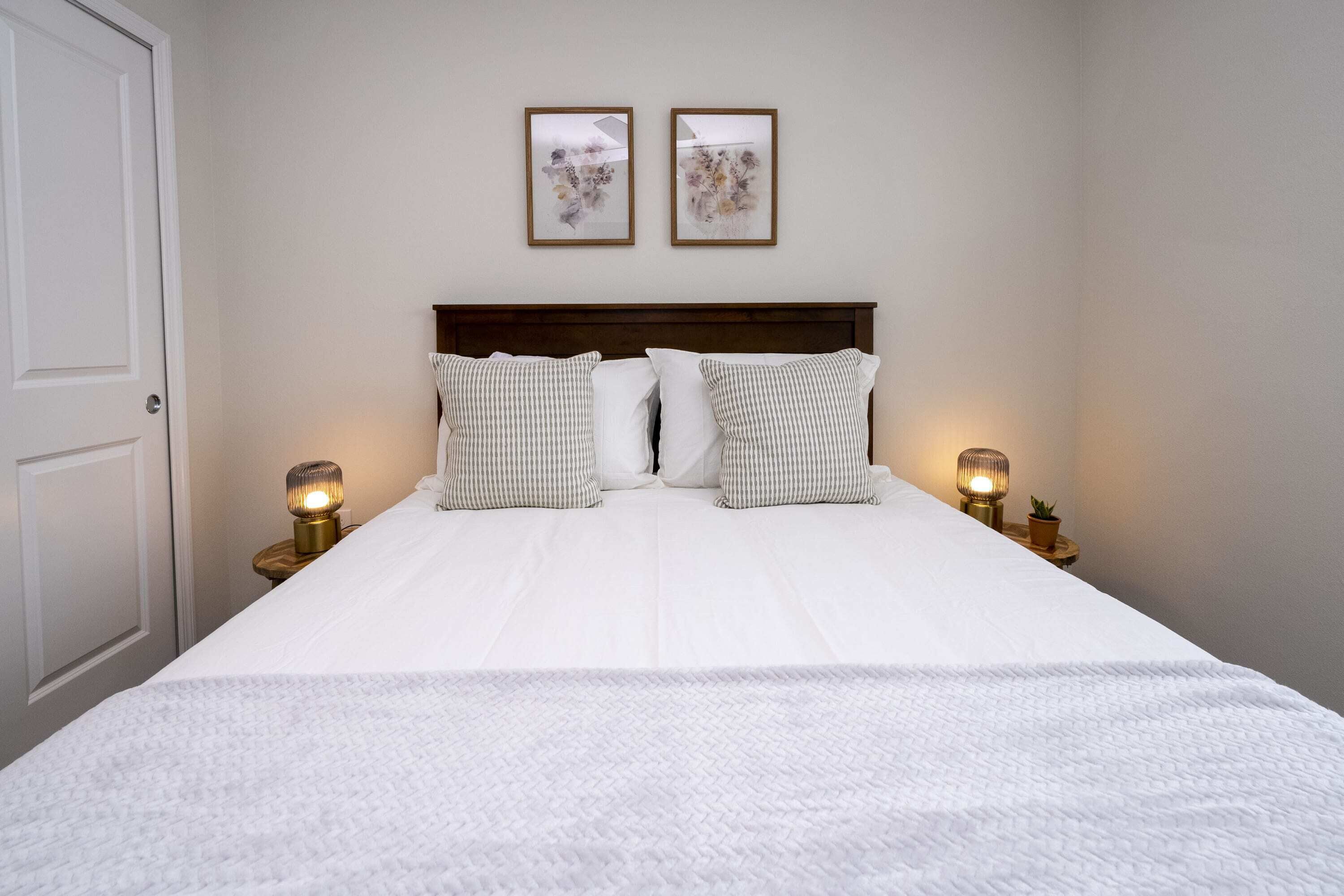 A neatly made bed with a white duvet, two pillows, and two bedside lamps on wooden nightstands.