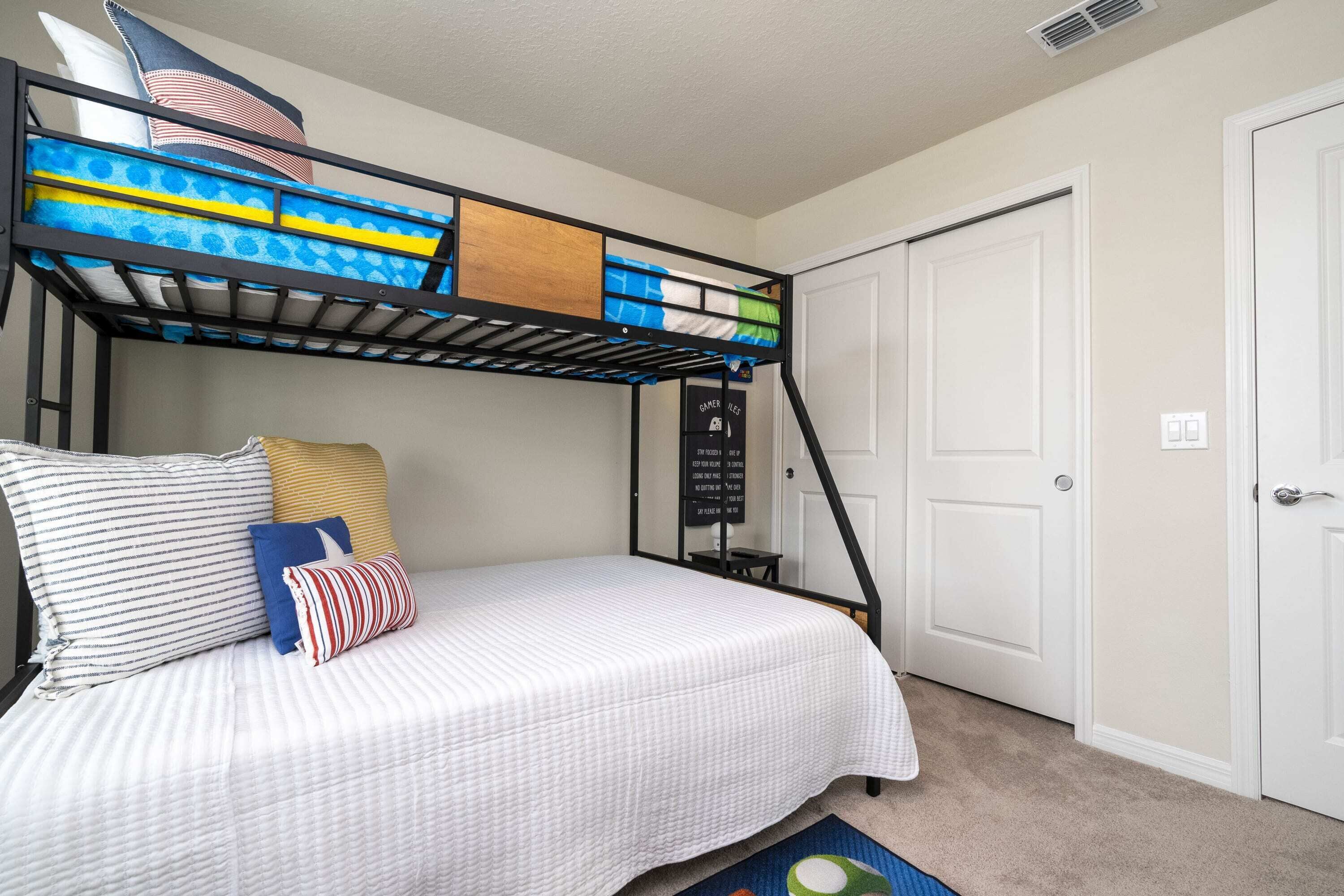 A bunk bed with a white mattress and blue and yellow bedding. There is a white door and a small blackboard with writing on it.