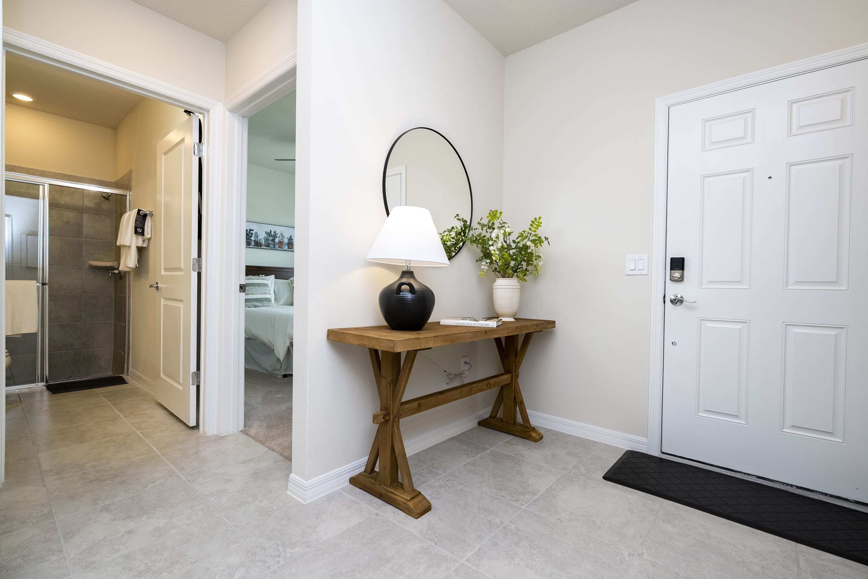 A hallway with a wooden console table, a mirror, a potted plant, and a white door.