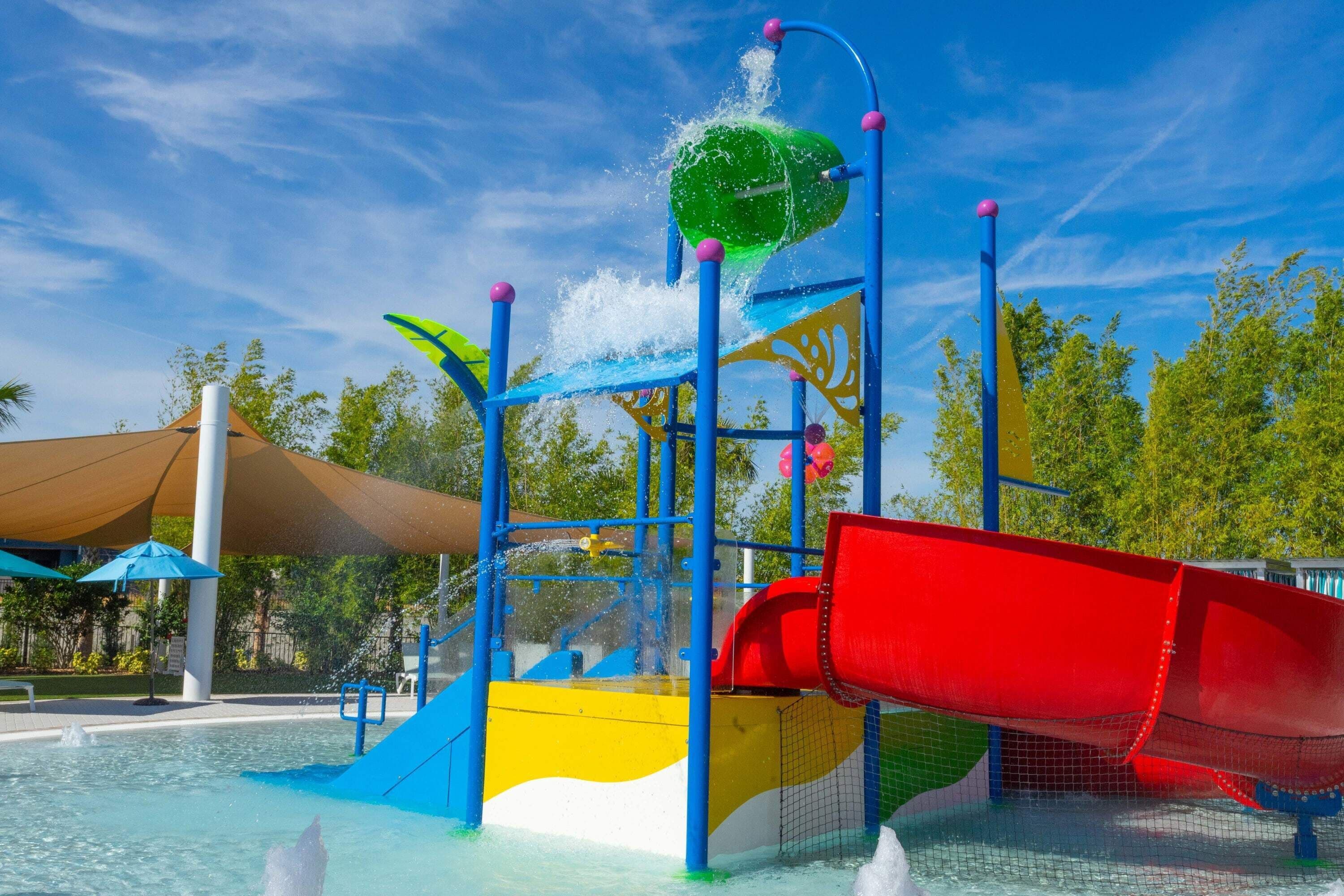 Parque acuático con un tobogán rojo, una fuente de agua y una estructura de juegos.