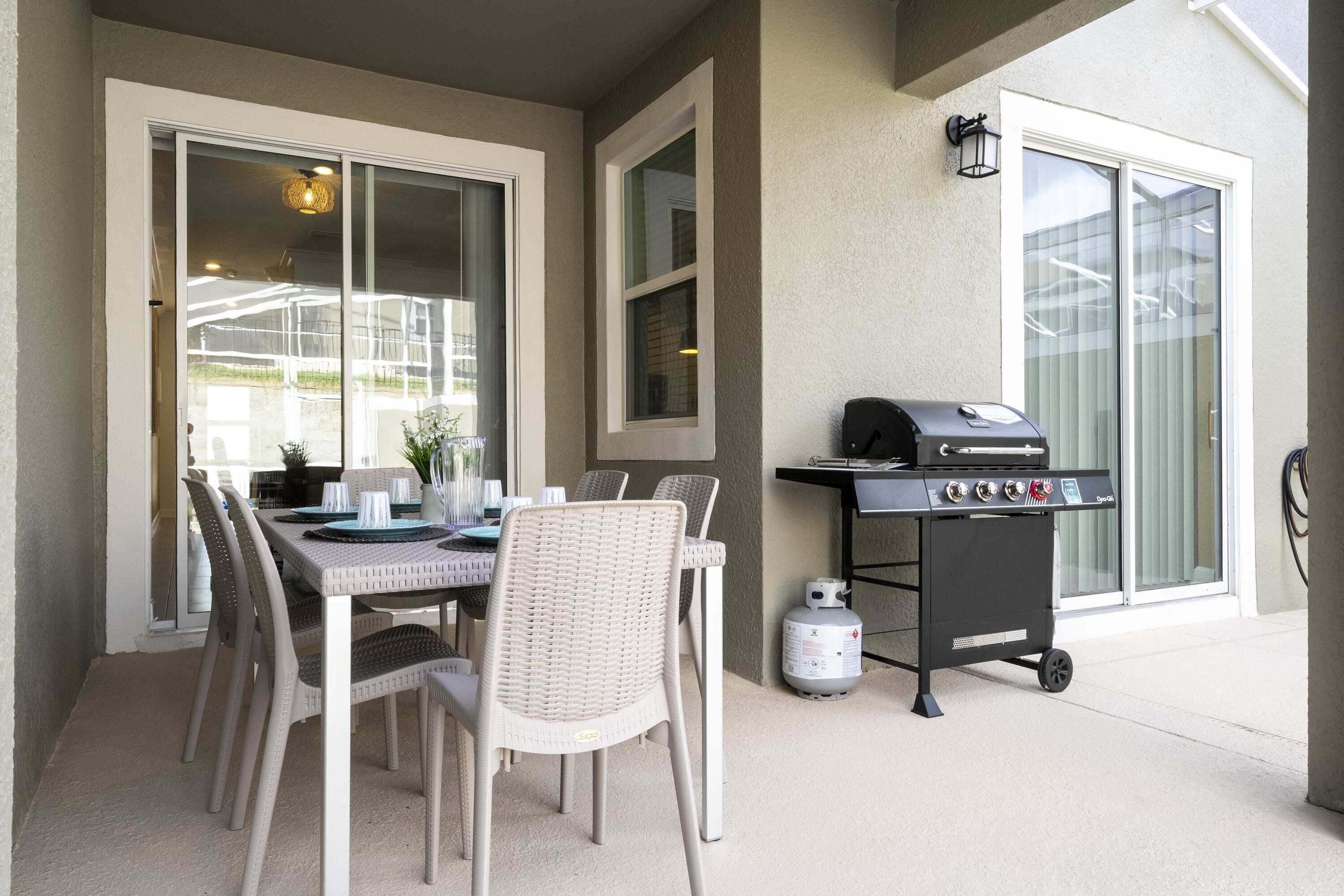 An outdoor patio with a table and chairs, a grill, and a propane tank.