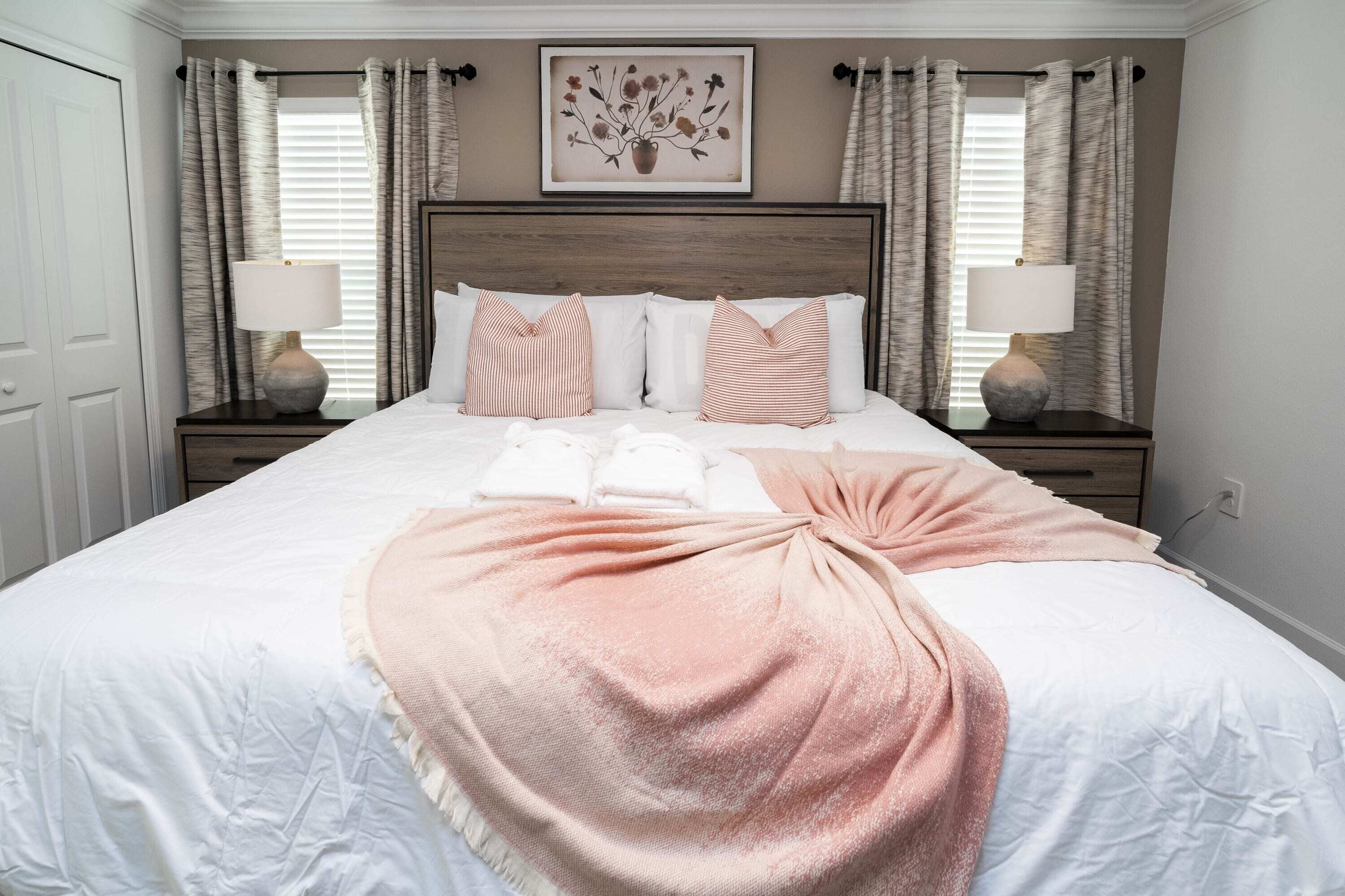 A neatly made bed with a pink throw, white pillows, and a framed artwork above.