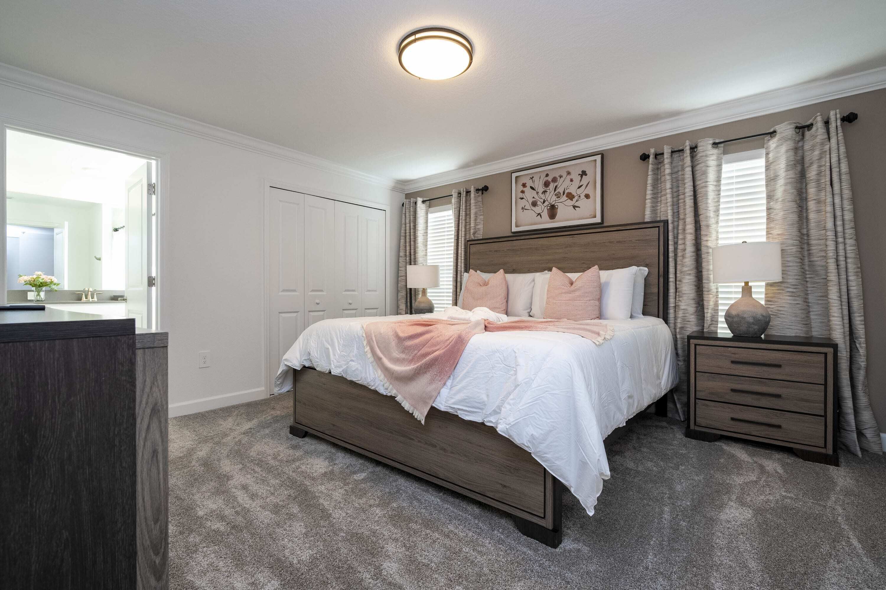 A bedroom with a bed, bedside tables, a headboard, a window with curtains, and a door.