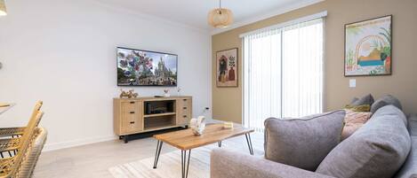A living room with a sofa, a wooden coffee table, a TV, and a dining area with wicker chairs.