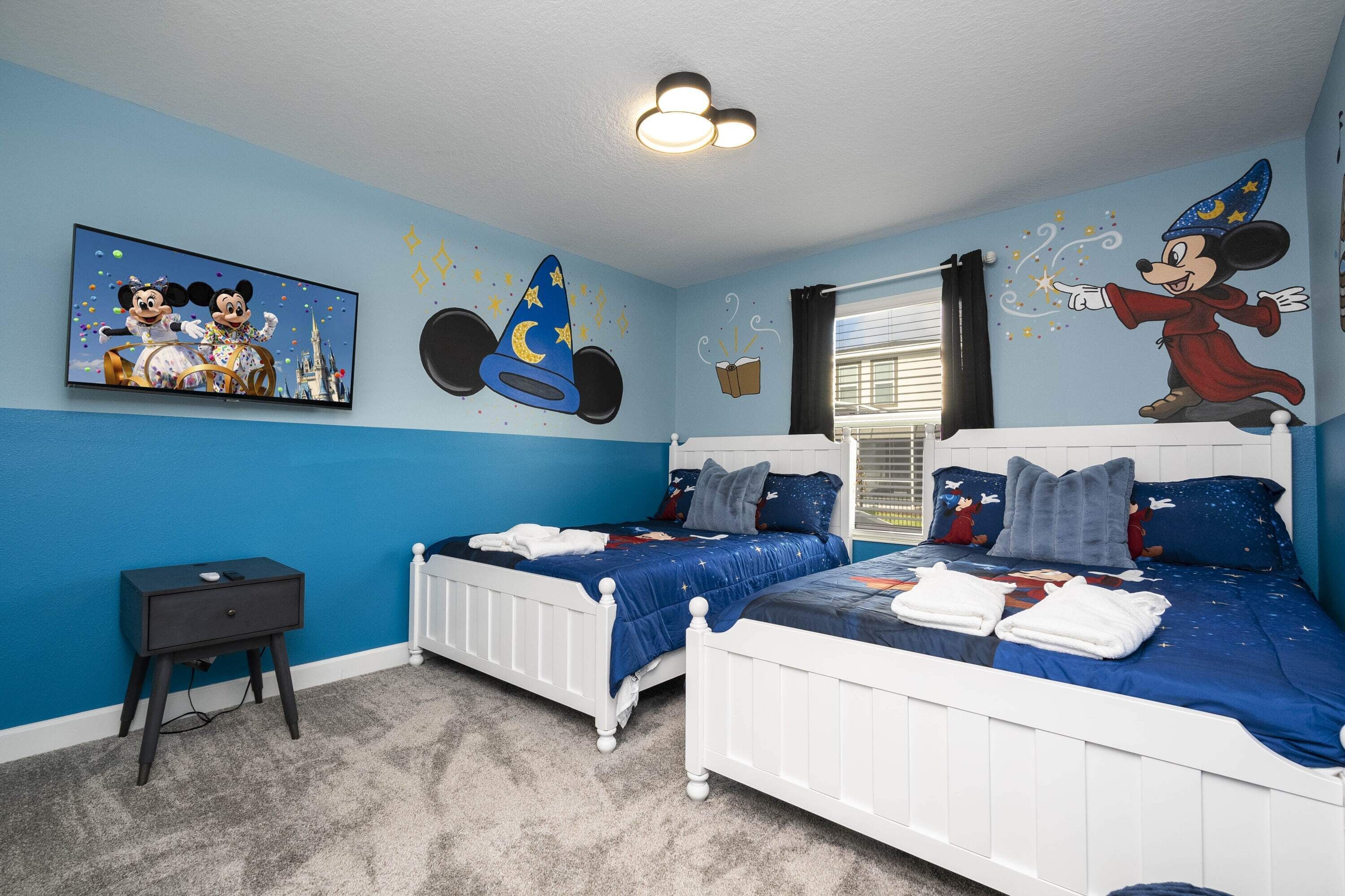 Un dormitorio infantil con dos camas, una mesita de noche y decoración temática de Mickey Mouse.