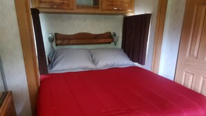 Un llit amb una colcha vermella i dos coixins, amb un capçal de fusta i una petita estanteta a sobre.