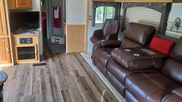 Interior acollidor d'una caravana amb un sofà de cuir, armaris de fusta i una televisió.