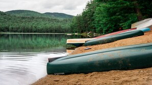 A row of canoes on a sandy shore by a calm lake with a forested hill in the background. - Sweet Chalet by the Lake! (Stony Creek)