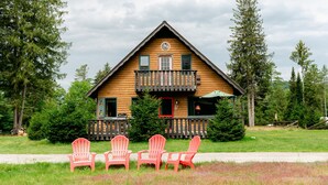 A log cabin with a balcony, surrounded by trees and featuring four red Adirondack chairs in front. - Sweet Chalet by the Lake! (Stony Creek)