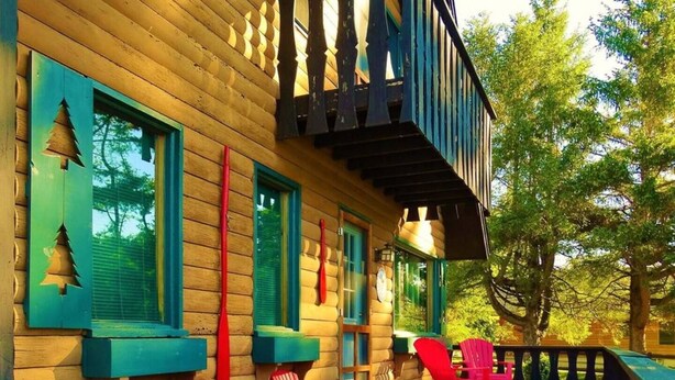 A wooden cabin with a deck, red chairs, and green window shutters. - Sweet Chalet by the Lake! (Stony Creek)