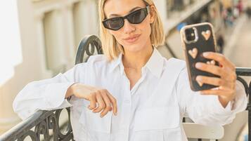 A person seated at a table with a smartphone, a cup of coffee, and a metal railing in the background.