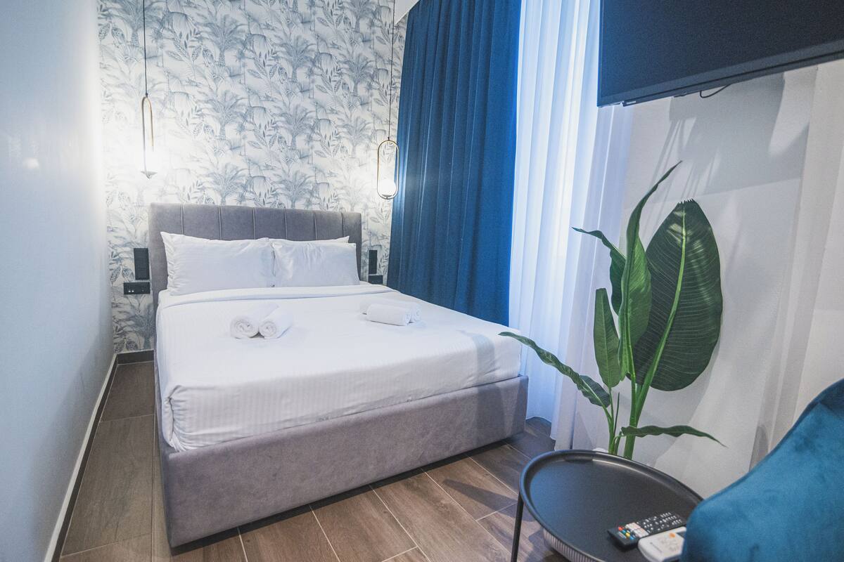 A neatly made bed with white linens, a grey headboard, and a bedside table with a remote control.