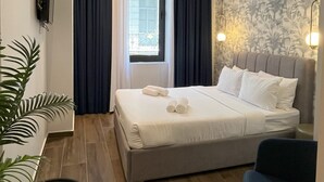 Ett välordnat hotellrum med en säng, ett litet bord, en stol och en krukväxt.