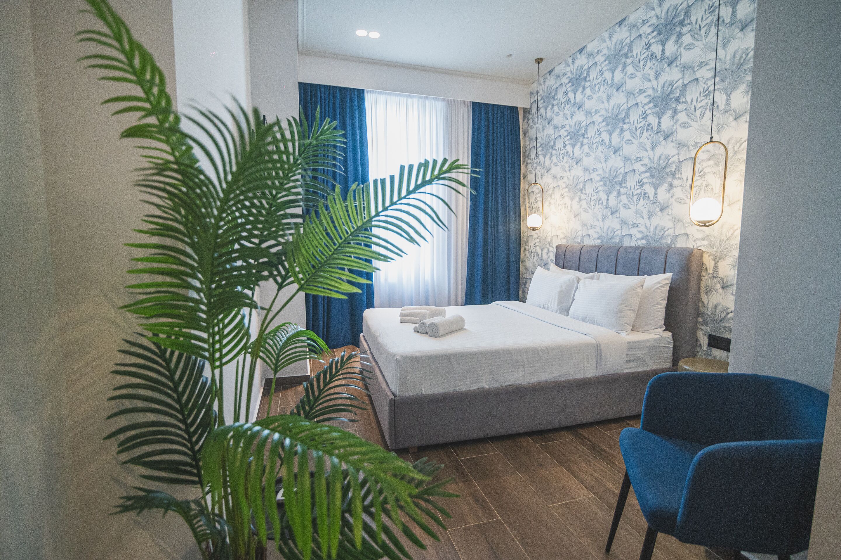 A hotel room with a bed, a blue chair, and a large plant.