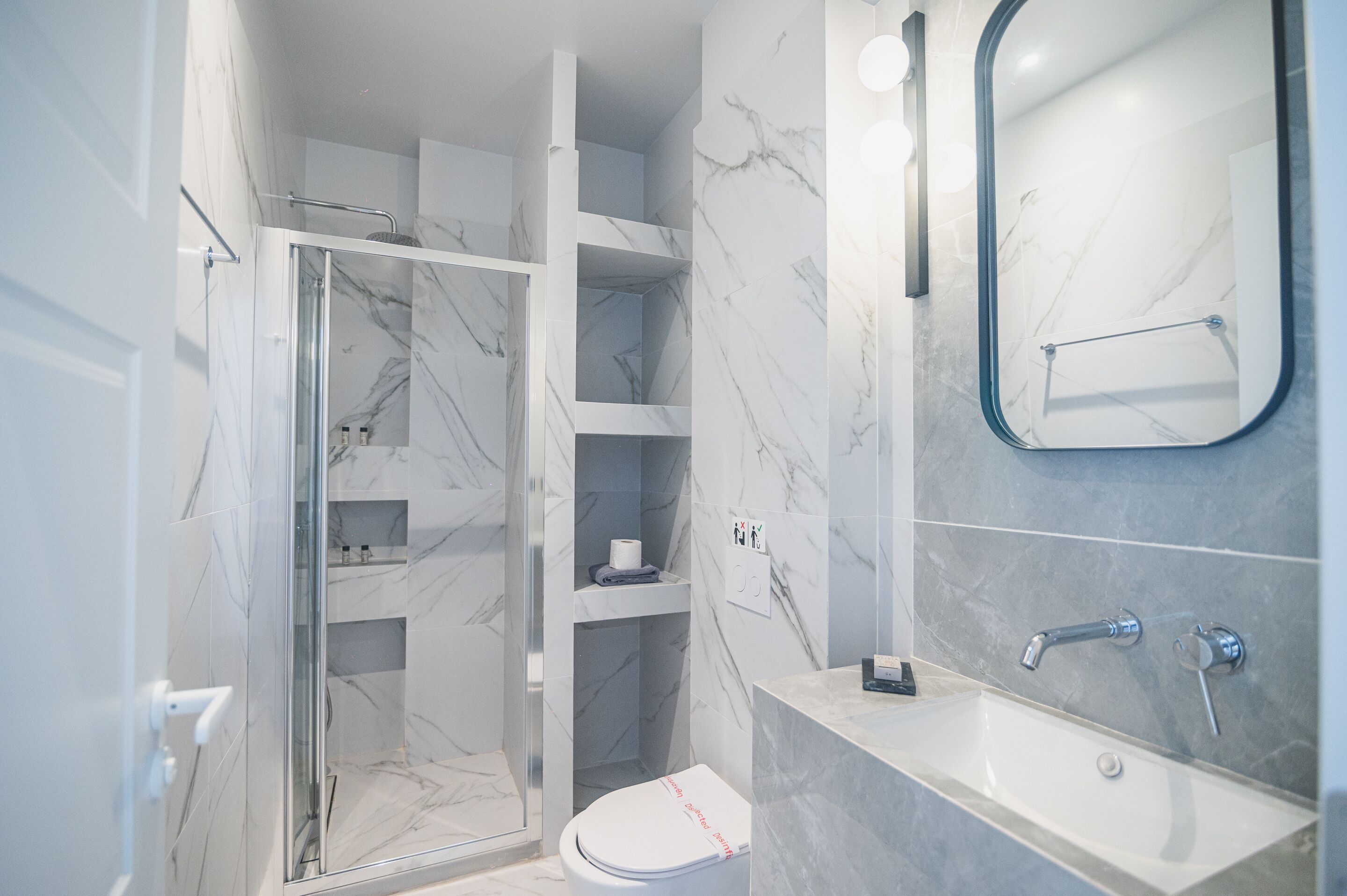 A modern bathroom with a glass-enclosed shower, a white toilet, a marble-tiled sink, and a mirror.