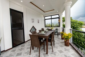 Un coin repas comprenant une table et des chaises, une grande fenêtre et un balcon agrémenté de plantes.