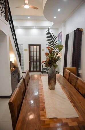 Un coin repas avec une table en bois, des bancs, un vase de fleurs et un escalier.