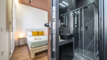 Una camera d'albergo moderna con un letto, un comodino e un angolo doccia con porta in vetro.