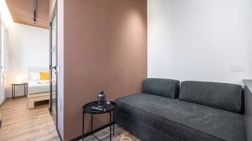 Una camera moderna con un divano grigio, un tavolino rotondo con una lampada e un letto con testiera bianca.