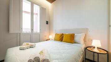 Una camera d'albergo con un letto, due lampade da comodino, una finestra con tende e una porta.