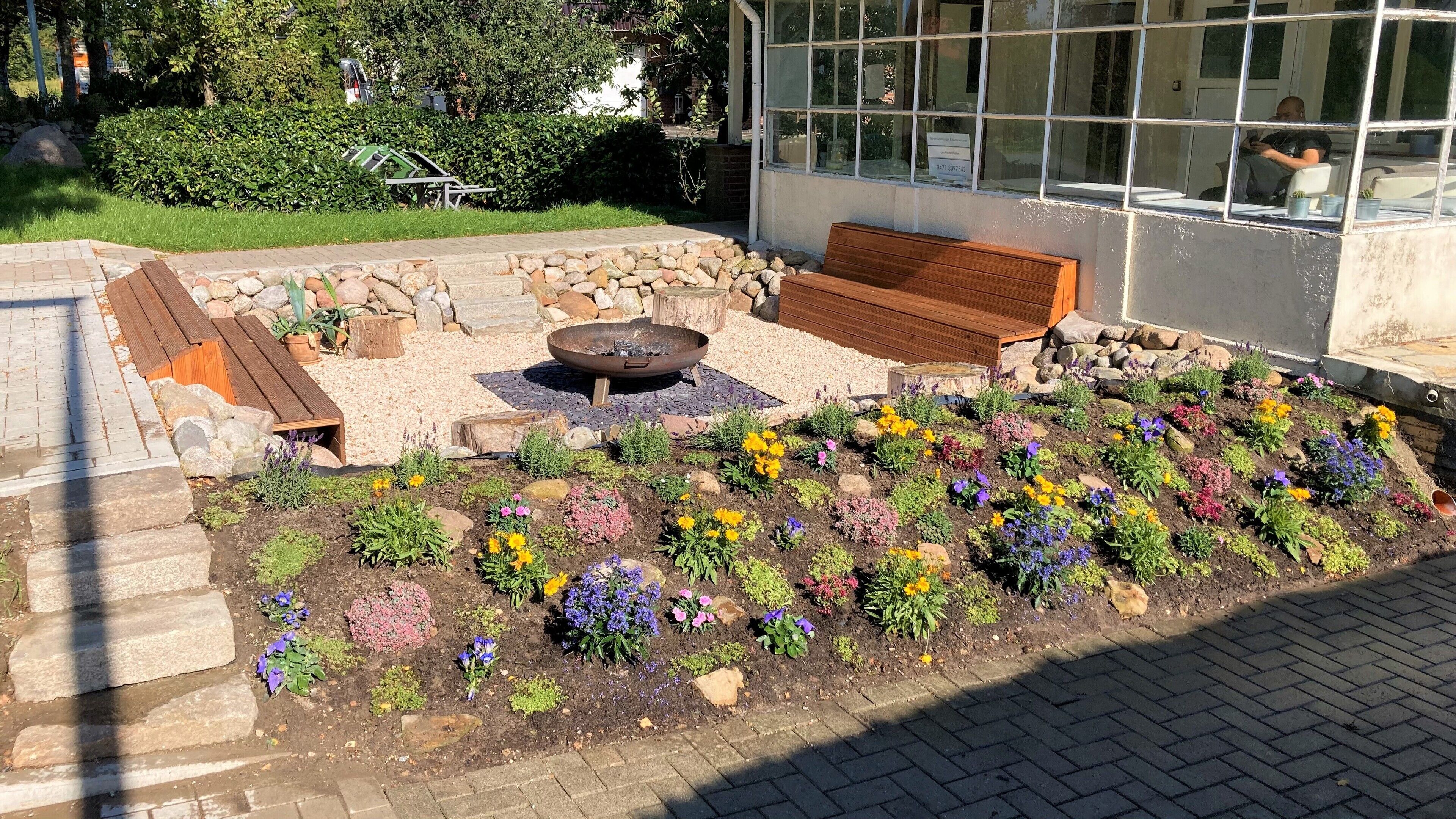 A garden area with a fire pit, wooden bench, and a variety of colorful flowers.