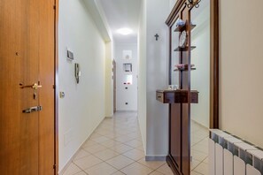 Un couloir avec une porte en bois, un téléphone fixé au mur, un radiateur et une étagère ornée d’objets décoratifs.