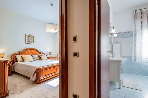 Une chambre à coucher avec un lit en bois, une table de chevet, une commode, un luminaire suspendu et un tableau encadré au mur.