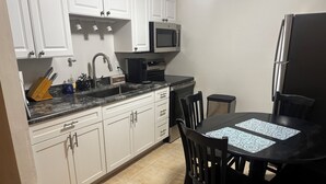 Une cuisine compacte avec des meubles blancs, un plan de travail noir, un four à micro-ondes, un réfrigérateur et une table à manger avec des chaises.