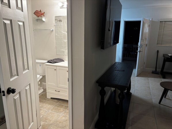 A hallway with a white door, a bathroom with a shower, and a dining area with a table and chairs. - Redington Escape Unit A - Just Steps from the Beach! (Redington Shores)
