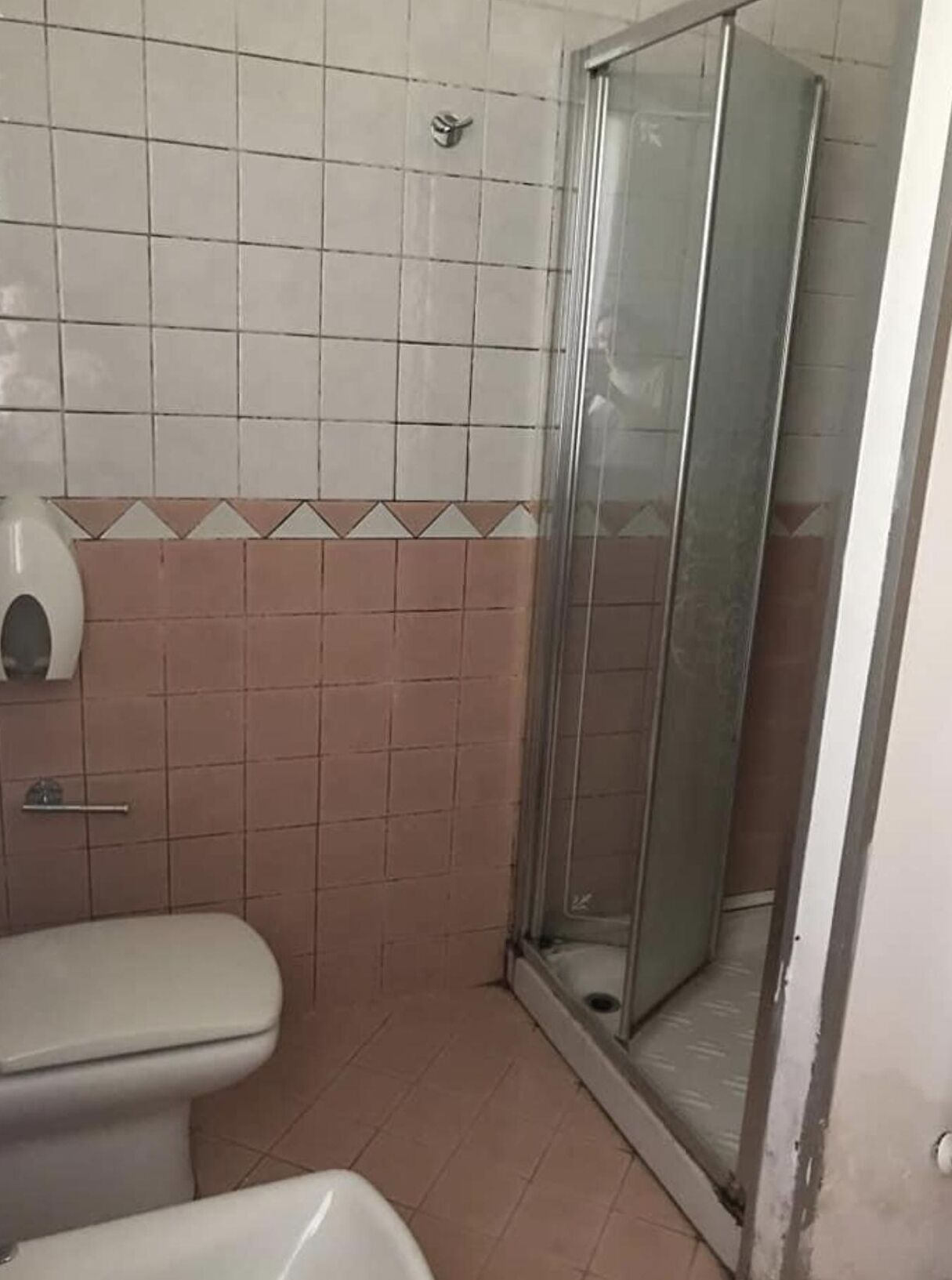 Pieni kylpyhuone, jossa on wc, käsienkuivaaja ja lasinen suihkuseinä.