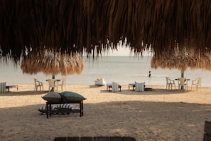 A beach setting with thatched umbrellas, lounge chairs, and a table with cushions. - Isla Baru (Cartagena)