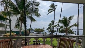 Een balkon met een houten tafel en stoelen, met uitzicht op een kustgebied met palmbomen en zee.