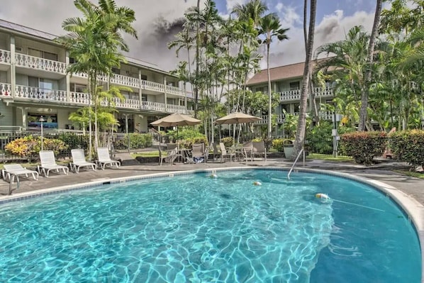 A hotel pool area with clear blue water, surrounded by palm trees and lounge chairs.