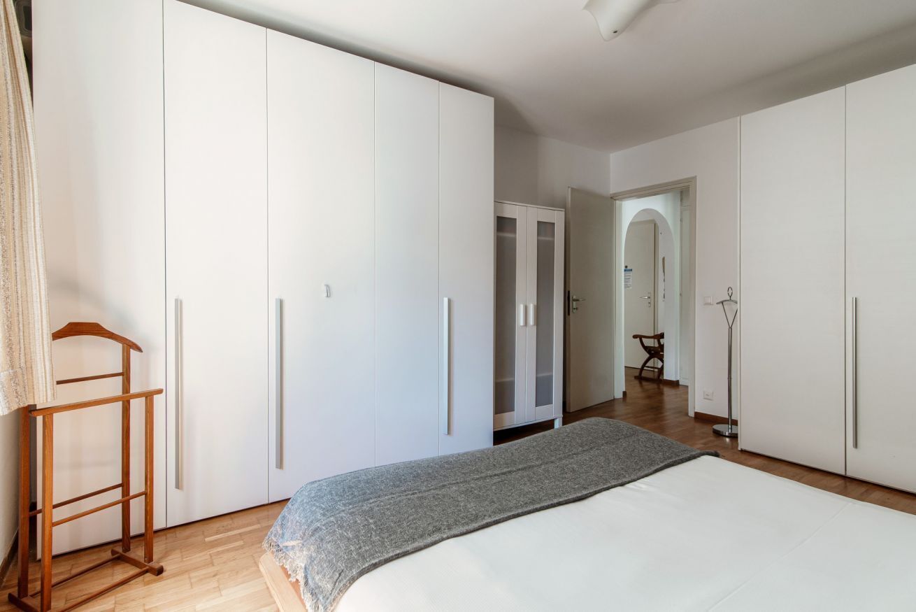 A bedroom with a large bed, white wardrobes, and a wooden hanger.