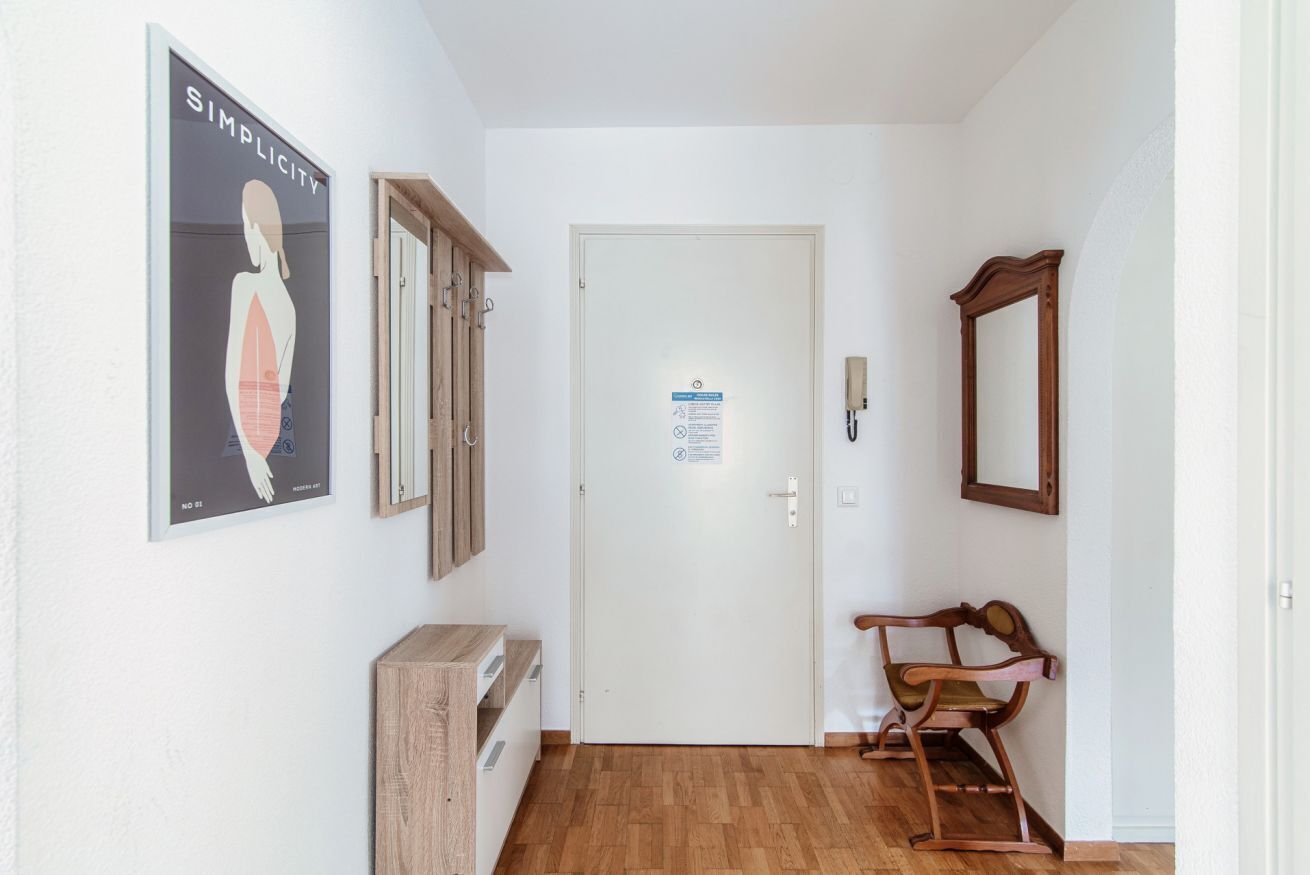 Un couloir avec un plancher en bois, une porte blanche avec une pancarte, un banc en bois et un tableau encadré accroché au mur.