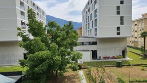 A modern building with a large tree in front, a grassy area, and a mountain in the background. - Apartment 5 minutes from Locarno Centro (Victoria Apartment) (Solduno)
