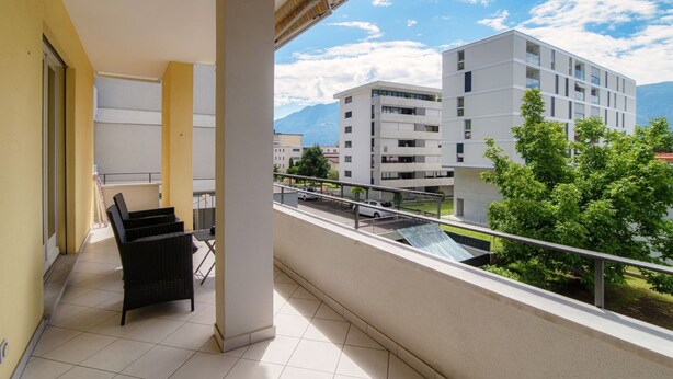 A balcony with a view of modern buildings and mountains. - Apartment 5 minutes from Locarno Centro (Victoria Apartment) (Solduno)
