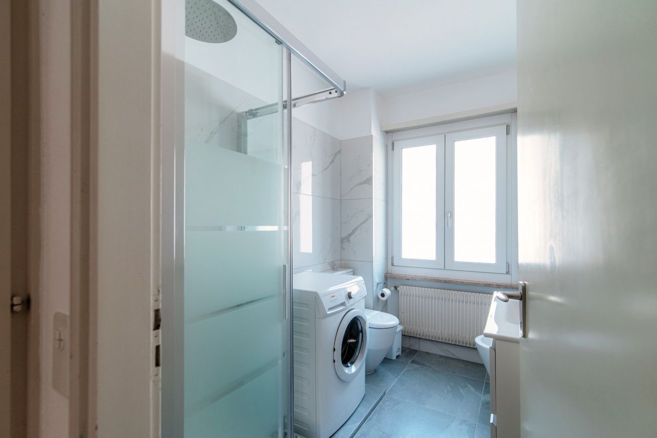 Une salle de bain moderne avec une douche à parois de verre, un lave-linge et des toilettes.