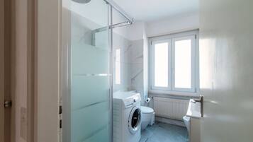 Une salle de bain moderne avec une douche à parois de verre, un lave-linge et des toilettes.