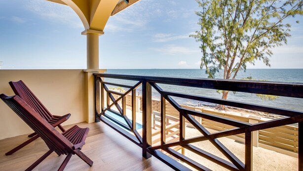 A balcony with wooden railings, a wooden floor, and a view of the sea and beach.