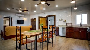 A modern kitchen with wooden cabinets, a dining table with chairs, a ceiling fan, recessed lighting, and a TV mounted on the wall.