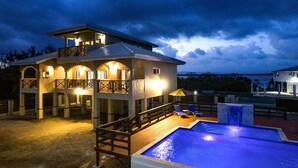 A two-story house with a pool, outdoor lighting, and a view of the ocean.