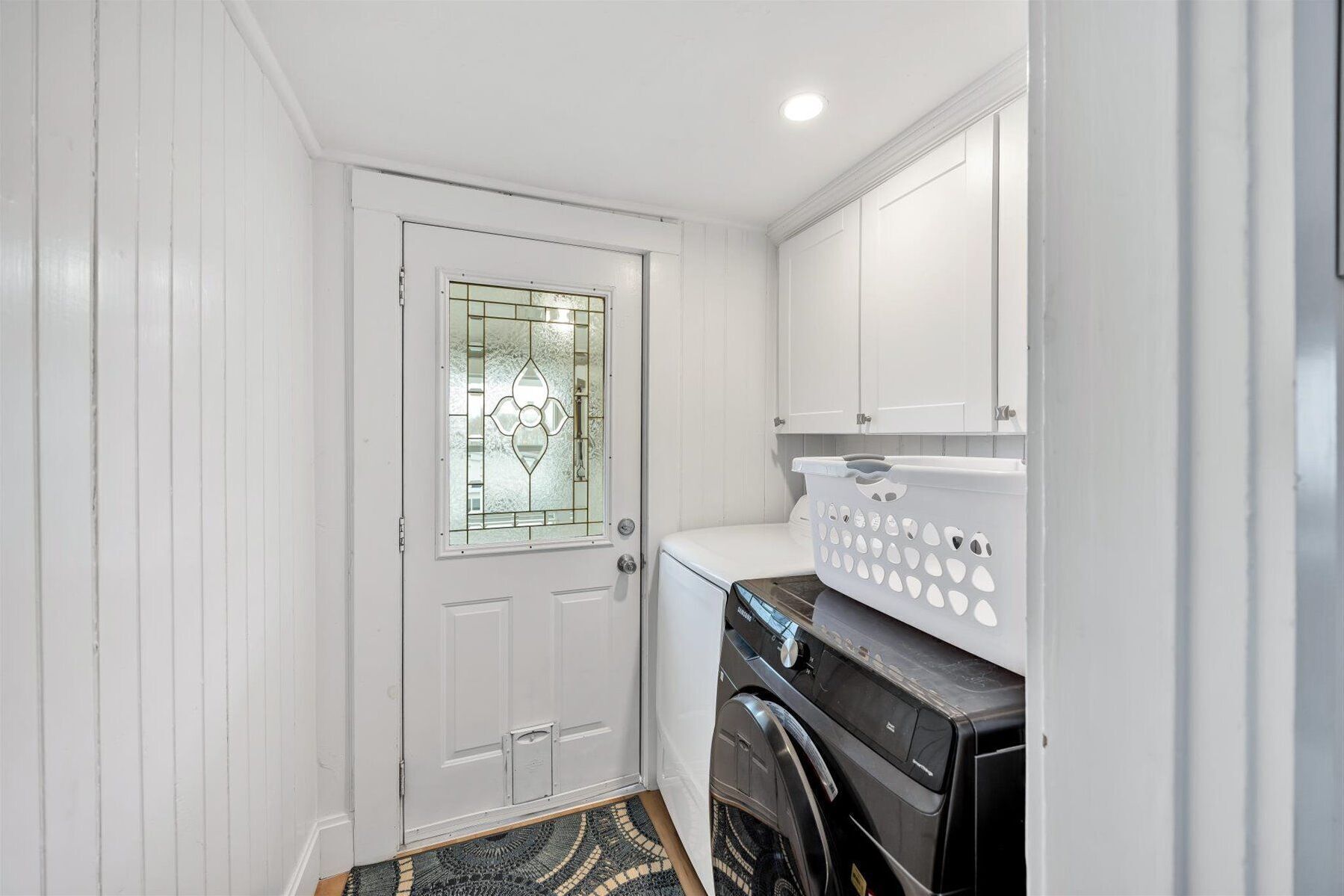 A compact laundry room with a washing machine, a dryer, and a door with a frosted glass panel.