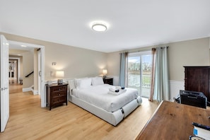 Une chambre à coucher comprenant un lit, des tables de chevet, un bureau et donnant sur l’extérieur.