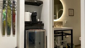 A compact kitchen with a refrigerator, a coffee machine, and a sink with a mirror above it. There is a small shelf with decorative items and a hanging rack with towels. - Wine Country Trail, View, Gated property, Detached Studio & Private View Patio, (Paso Robles)