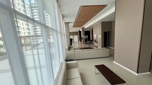 Eine großzügige Lobby mit einer modernen Couch und einer Holzbank, großen Fenstern und Blick auf Gebäude.