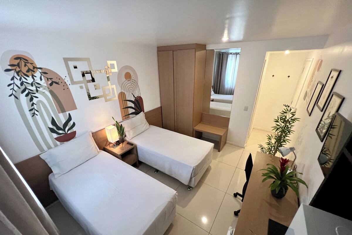 Habitación de hotel con dos camas, un escritorio, una silla, una lámpara y una planta en maceta.