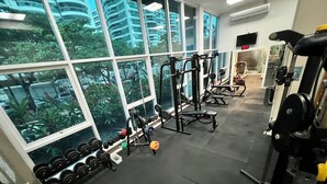 Ein Fitnessstudio mit unterschiedlichen Trainingsgeräten, großen Fenstern und Blick auf Gebäude und Bäume.